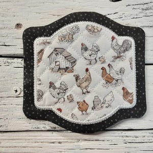 May include: A black and white quilted hot pad with a farmhouse theme. The pad features a white background with a black border and a variety of images including chickens, a coop, and eggs.