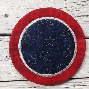 May include: A red, white, and blue fabric coaster with a star pattern. The coaster is round and has a white border.