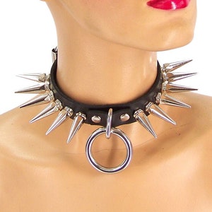 May include: A black leather choker with silver spikes and a large silver ring. The choker is worn by a mannequin with a bald head and red lipstick.