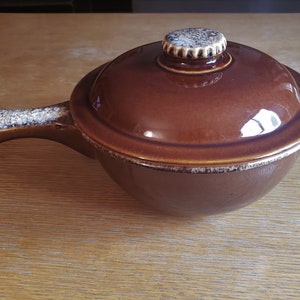 May include: A brown ceramic casserole dish with a lid and a handle. The dish has a speckled glaze.