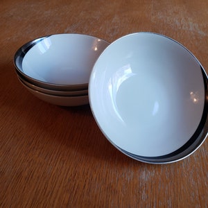 May include: Three white ceramic bowls with a black and silver rim. The bowls are stacked on top of each other.