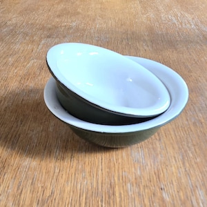 May include: Two stacked bowls with a dark olive green exterior and a smooth white interior. The bowls feature a rounded shape and a dark rim, showcasing a clean design with a glossy finish that reflects light on the inner surface.