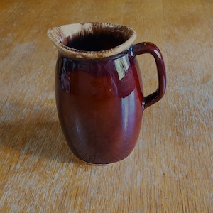 May include: A brown ceramic pitcher with a white glaze on the rim. The pitcher has a rounded body and a handle.