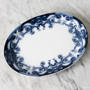 May include: Oval white and blue ceramic serving dish. The dish features a white center with a blue floral and scroll design around the rim. The rim is a dark blue color. The dish is on a marble surface.