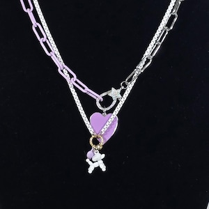 May include: A layered necklace with a purple heart pendant and a small white dog charm. The necklace features a combination of silver and purple chain links, and a star-shaped clasp. The jewelry is displayed on a black mannequin.