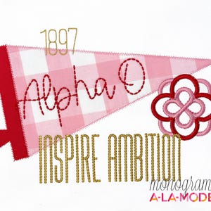 May include: A red and white pennant with the text "Alpha O" and "Inspire Ambition" in gold thread. A red and pink floral design is on the right. The year "1897" is above the pennant.