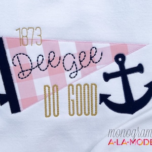May include: White fabric with an embroidered nautical design. Features a pink and white gingham pennant with the name "Dee Gee" and the words "Do Good". Includes a navy anchor and the year "1873" in gold thread.
