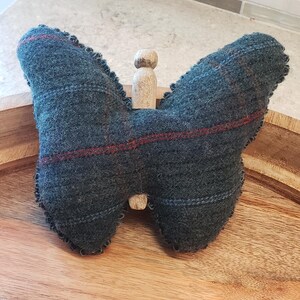 Pode incluir: Um almofadinha para alfinetes em forma de borboleta azul e vermelha xadrez com um pino de madeira no centro. O almofadinha est&aacute; sobre uma superf&iacute;cie de madeira.