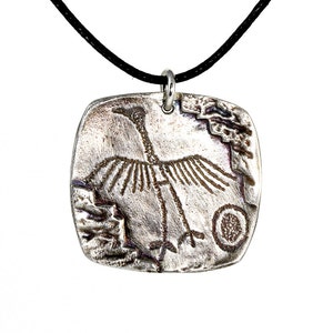 May include: A silver pendant necklace with a black cord. The pendant is square shaped and features an etched design of a bird with outstretched wings.
