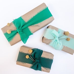 May include: Three brown gift boxes wrapped with green and blue ribbon and decorated with small dried flower buds.