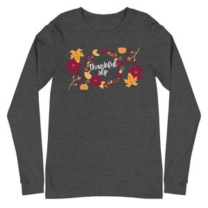 Può includere: Una maglietta a maniche lunghe color grigio scuro melange con un design a corona di fiori e il testo "thankful slp" in bianco.