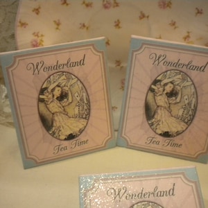 May include: Three pastel blue and pink paper signs with the text "Wonderland Tea Time" and an illustration of Alice in Wonderland.