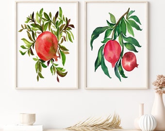 Puede incluir: Dos acuarelas de ramas de granadas con frutos rojos y hojas verdes. Las pinturas están enmarcadas en marcos de madera natural y se exhiben en una pared blanca.