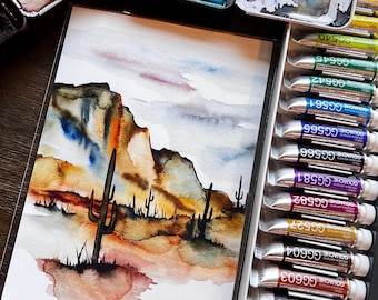 May include: A watercolor painting of a desert landscape featuring saguaro cacti and rocky formations in shades of orange, brown, and blue, positioned next to a set of Holbein gouache paint tubes and a metal palette with dried paint.