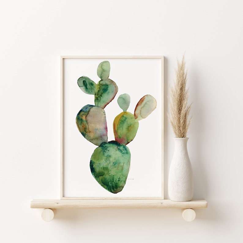 May include: A watercolor painting of a green cactus with a white background. The cactus is in a simple wooden frame and is on a shelf with a vase of dried grass.