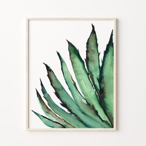 May include: Watercolor painting of a green agave plant in a light wood frame. The artwork features shades of green and brown, with a focus on the plant's spiky leaves. The painting is set against a white background, creating a minimalist aesthetic.