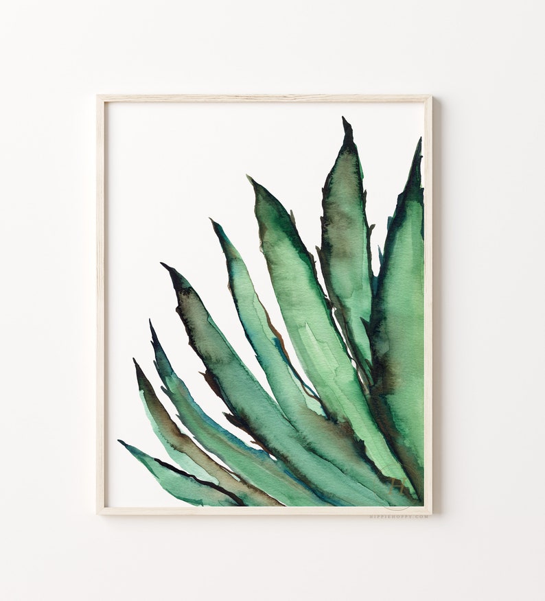 May include: Watercolor painting of a green agave plant in a light wood frame. The artwork features shades of green and brown, with a focus on the plant's spiky leaves. The painting is set against a white background, creating a minimalist aesthetic.