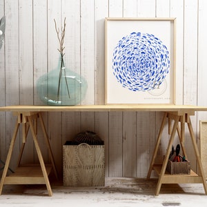 May include: A framed print of a blue watercolor painting of a circle of fish on a white background. The print is hanging on a white wall above a wooden table with two sawhorses.