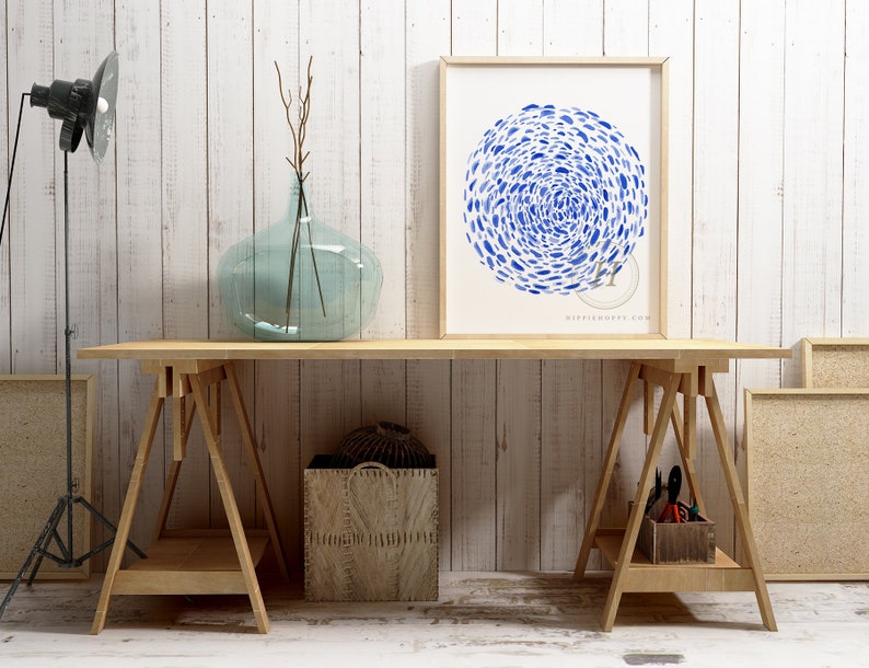 May include: A framed print of a blue watercolor painting of a circle of fish on a white background. The print is hanging on a white wall above a wooden table with two sawhorses.