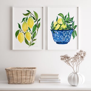 May include: Two framed watercolor paintings of lemons. The first painting shows a branch of lemons with green leaves. The second painting shows a blue and white bowl filled with lemons.