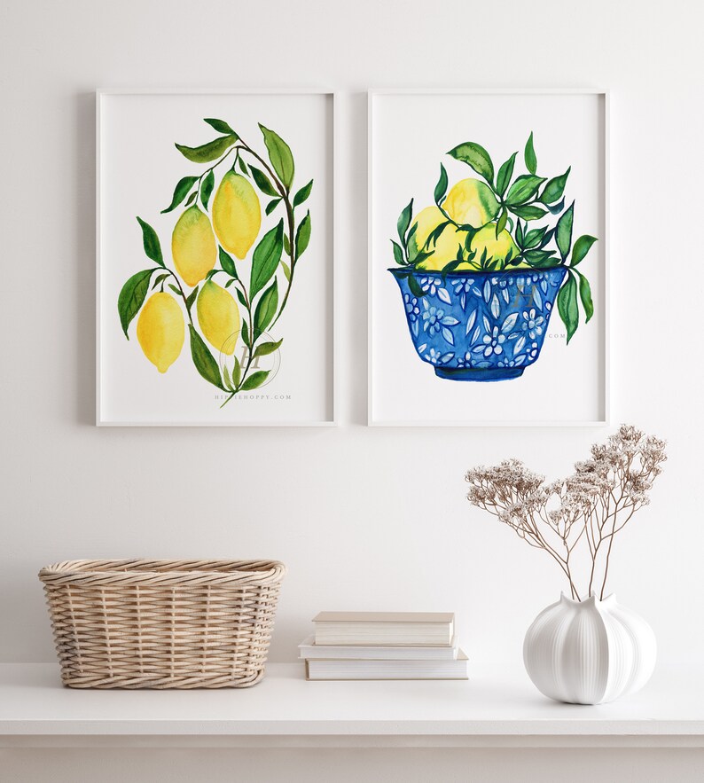 May include: Two framed watercolor paintings of lemons. The first painting shows a branch of lemons with green leaves. The second painting shows a blue and white bowl filled with lemons.