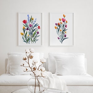 May include: Two framed watercolour paintings of floral bouquets. The paintings are in a minimalist style with white backgrounds and feature colourful flowers in shades of pink, red, orange, yellow, and blue.