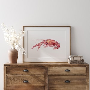 May include: A watercolor painting of a red crawfish in a wooden frame. The painting is on a wooden dresser with a vase of white flowers.