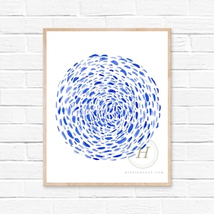 May include: A blue and white abstract watercolor print with a circular design of small blue dots. The print is framed in a light wood frame.