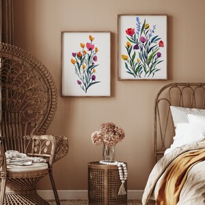 May include: Two framed watercolour paintings of colourful floral bouquets with green leaves and stems. The paintings are hanging on a light brown wall above a wicker chair and a wicker bed frame.