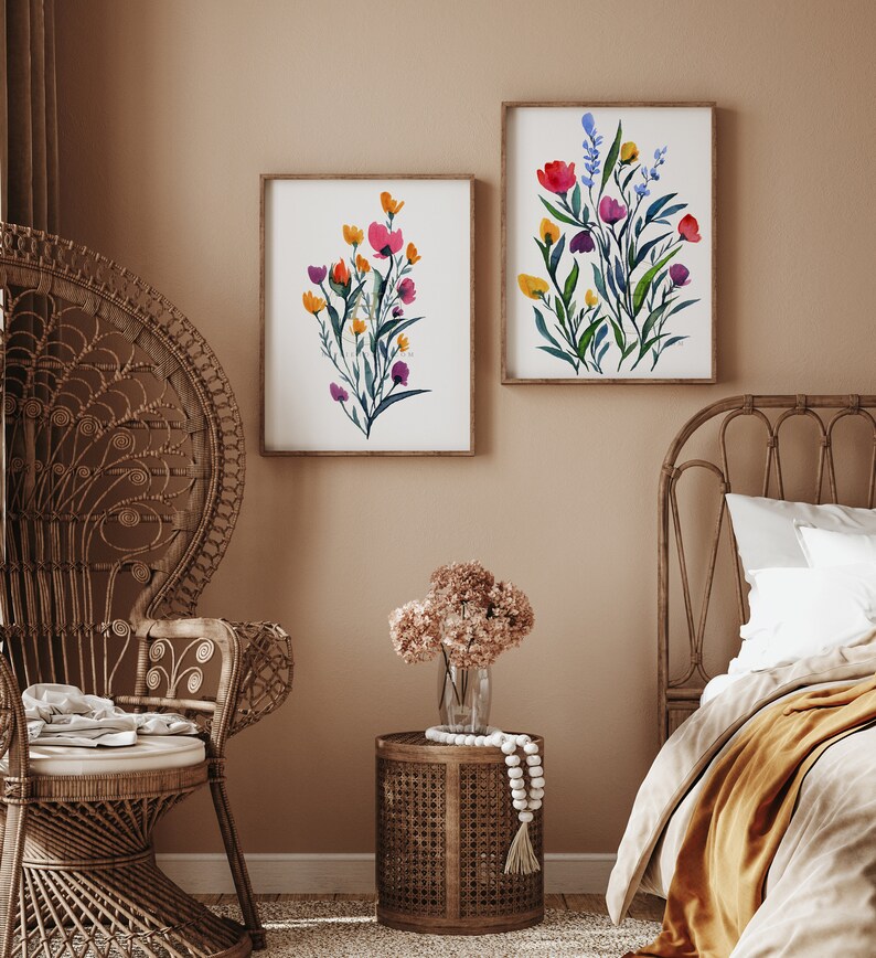 May include: Two framed watercolour paintings of colourful floral bouquets with green leaves and stems. The paintings are hanging on a light brown wall above a wicker chair and a wicker bed frame.