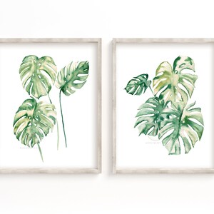 May include: Two framed watercolor paintings of green monstera leaves on a white background. The leaves are painted in shades of green and yellow.