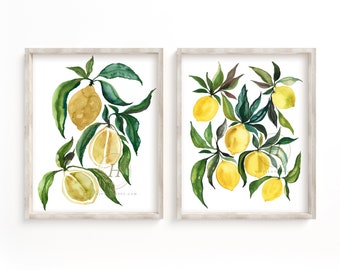 May include: Two framed watercolor paintings of lemon branches with green leaves and yellow lemons. The paintings are in simple white frames with a light wood finish.