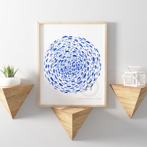 May include: A framed watercolor print of a blue abstract design with a swirling pattern of blue dots on a white background. The print is hanging on a white wall above a wooden shelf.