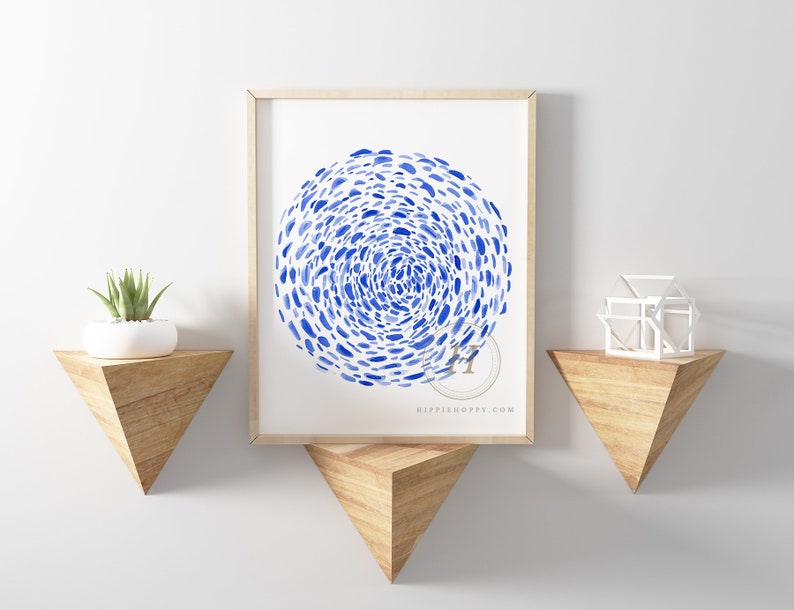 May include: A framed watercolor print of a blue abstract design with a swirling pattern of blue dots on a white background. The print is hanging on a white wall above a wooden shelf.