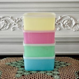 Peut inclure: Une pile de quatre boîtes de rangement rectangulaires en plastique avec couvercles. Les boîtes sont empilées verticalement, avec une boîte jaune clair au sommet, suivie d'une rose, d'une vert clair et d'une bleue claire à la base.