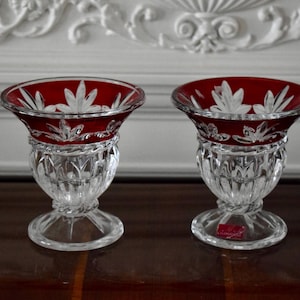 May include: Two clear glass vases with a red, cut-glass design. The vases have a wide, round base and a narrow, cylindrical neck.
