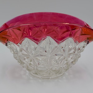May include: A clear glass bowl with a cut glass pattern and a red glass rim. The bowl is shaped like a scallop shell.
