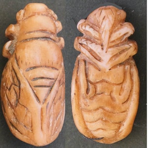 May include: Two carved, beige-coloured cicada charms. The charms are detailed with intricate carvings of the cicada's wings and body.