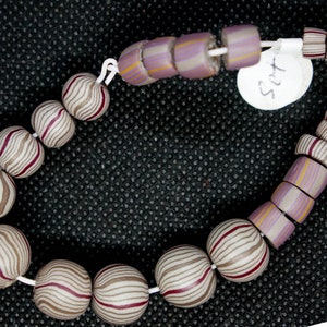 May include: A strand of vintage glass beads with a striped pattern in shades of brown, white, and pink. The beads are strung on a white cord and have a white tag with the word "Set" written on it.