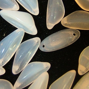 May include: A collection of translucent white and light pink glass beads in various shapes, including oval and teardrop. The beads have a smooth, polished finish.