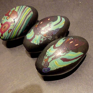 Könnte beinhalten: Drei schwarze Glasperlen mit bunten Wirbeln und Mustern. Die Perlen sind oval geformt und haben eine glänzende Oberfläche.