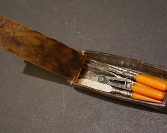 Antique miniature manicure set with coral handles.  Box looks like tortoise  shell but probably is plastic. Box slightly warped with use.