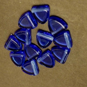 May include: A group of ten blue glass triangle beads with white stripes. The beads are arranged in a circle on a brown surface.