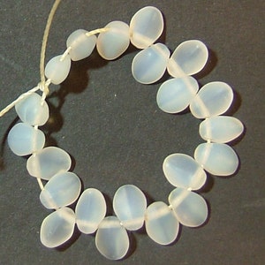May include: A strand of translucent white oval beads strung on a white thread. The beads are arranged in a circle.
