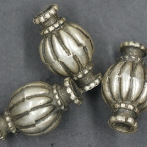 May include: Three silver metal beads with a decorative, ribbed design. The beads are round and have a slightly pointed top and bottom.