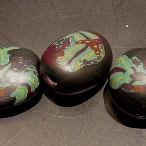 Könnte beinhalten: Drei ovale Glasperlen mit schwarzem Hintergrund und bunten Wirbeln in Grün, Rot und Braun.