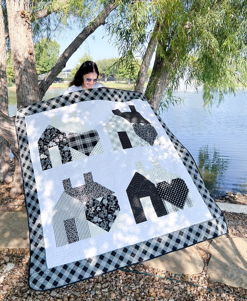 May include: A black and white quilt with a checkered border. The quilt features four houses with hearts in the center of each house. The houses are made of different fabrics with black and white patterns.