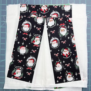 May include: A black and white fabric with a repeating pattern of Father Christmas figures and candy canes. The fabric is sewn into a pleated shape with white fabric on either side. The text "Don't forget to be good" is visible on the fabric.