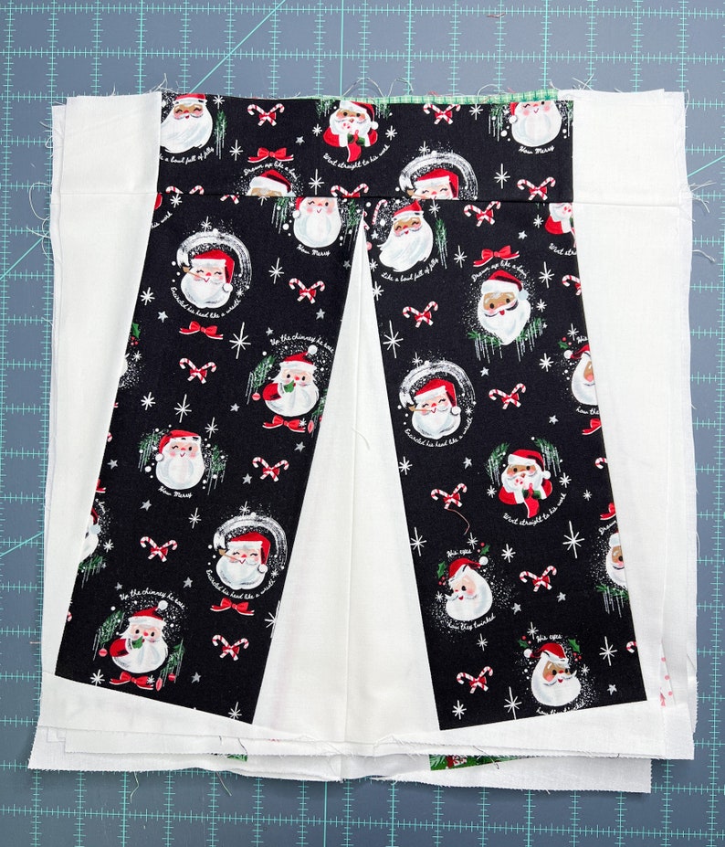 May include: A black and white fabric with a repeating pattern of Father Christmas figures and candy canes. The fabric is sewn into a pleated shape with white fabric on either side. The text "Don't forget to be good" is visible on the fabric.