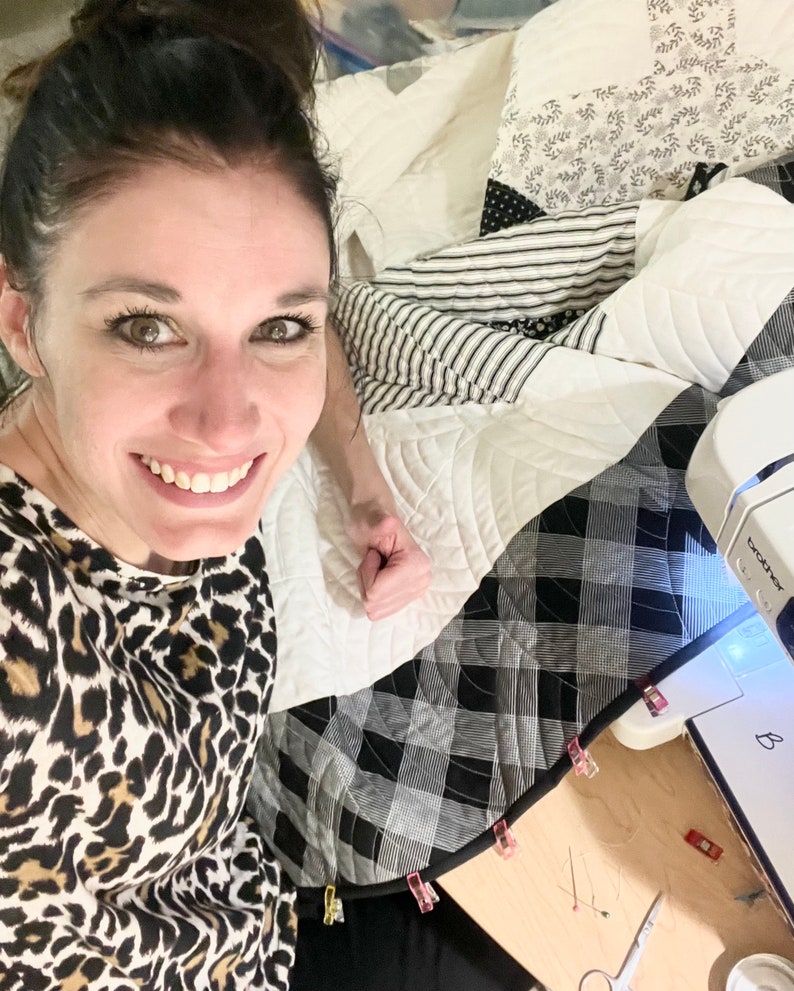 May include: A woman is sewing a quilt with a black and white checkered fabric. The quilt is being held in place with clips. The sewing machine is a Brother brand.